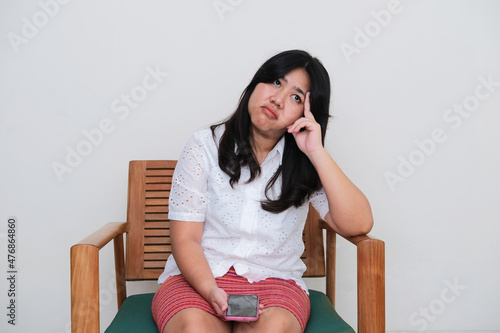 Adult Asian women sitting on the chair showing boring expression while holding mobile phone photo