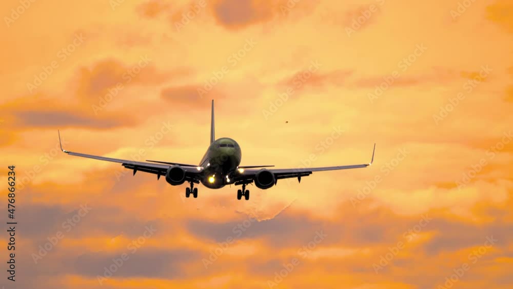 Silhouette of aircraft flying in orange sunset sky with clouds illuminated by setting sun. Gorgeous cloudscape with airplane. Flight of plane with flashing lights at sundown Silhouette of aircraft flying in orange sunset sky with clouds illuminated by setting sun. Gorgeous cloudscape with airplane. Flight of plane with flashing lights at sundown