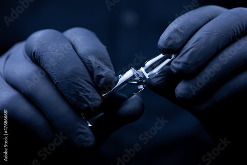 the hands of a doctor in black medical gloves are trying to break off the cap of an ampoule with a vaccine