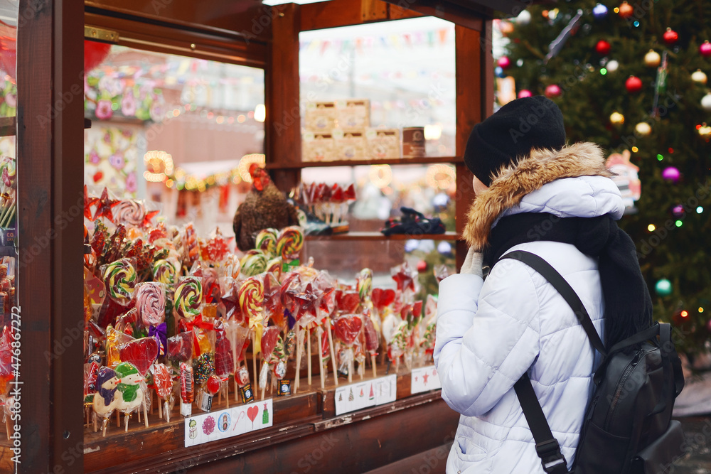 Outdoors in winter, a young woman from the back at the Christmas market walked to a display case with a lot of different lollipops to choose as a gift for her family and friends, copy space.