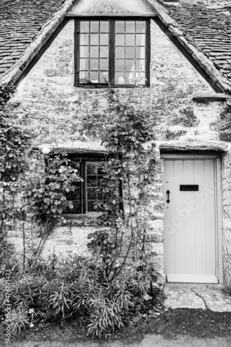 Facade of traditional small cottage home in Bibury village, Cotswolds, Egland, UK. Rurar house with wooden door and rose bushes photo