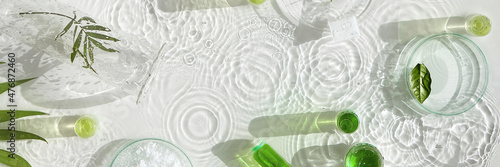 Cosmetic skincare background. Herbal medicine with green leaves. Natural sunlight, long shadows. Splashes of water, splashes. Chemical glassware, petri dishes, vials. Natural skincare background.