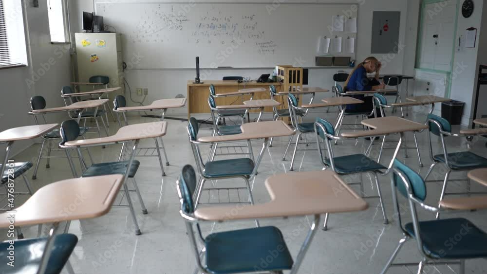Lone student works at her desk in a darkened empty school classroom. Lone student works at her desk in a darkened empty school classroom.