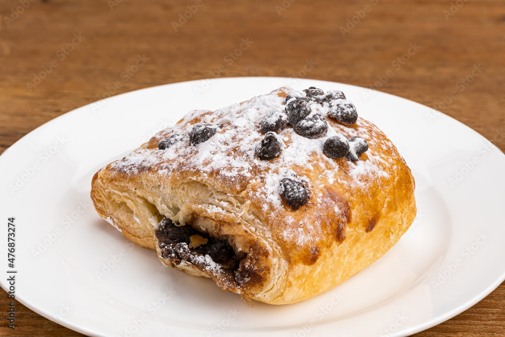 Danish Pasty filled with chocolate cream topping with chocolate chips and icing sugar in white ceramic dish on wooden table with clipping path. Danish Pasty filled with chocolate cream topping with chocolate chips and icing sugar in white ceramic dish on wooden table with clipping path.