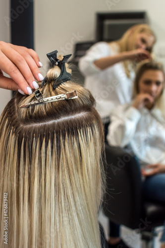 Hair extension process of a young woman in a beauty salon close-up. Vertical photography