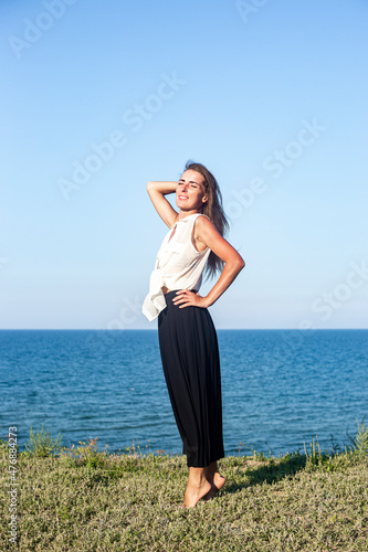 Fototapeta Naklejka Na Ścianę i Meble -  Beautiful young woman in a long black skirt posing while standing on a cliff