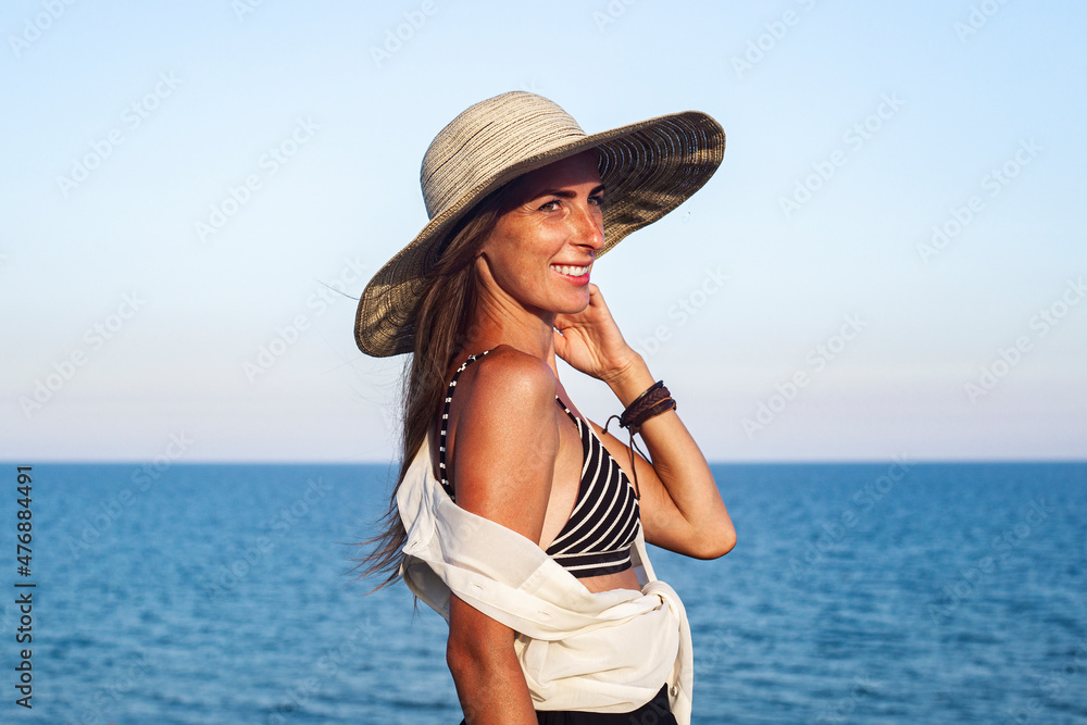 Smiling young woman in a hat on the background of the sea and sky.