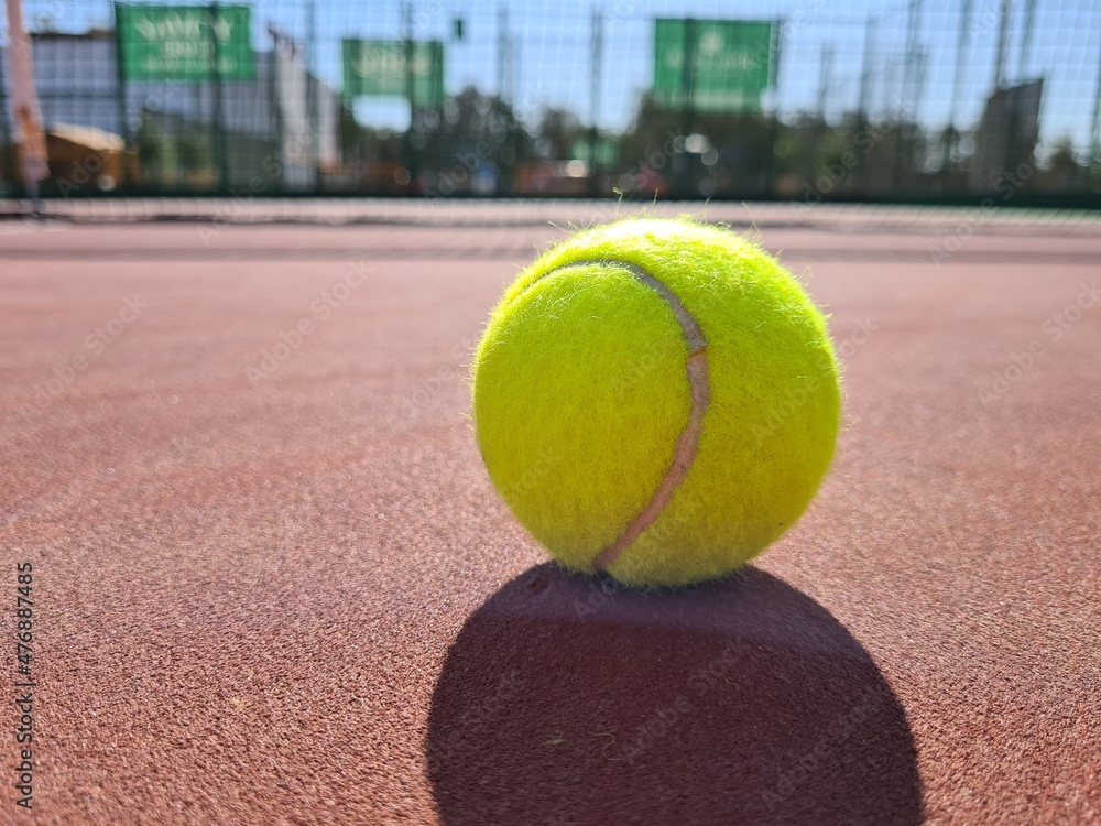 Tennis ball on the sunny red hard court. 