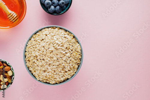 Oat flakes, blueberries, nuts and honey on a pink background. Dry oatmeal and dietary breakfast ingredients. Healthy breakfast concept. Copy space. Top view