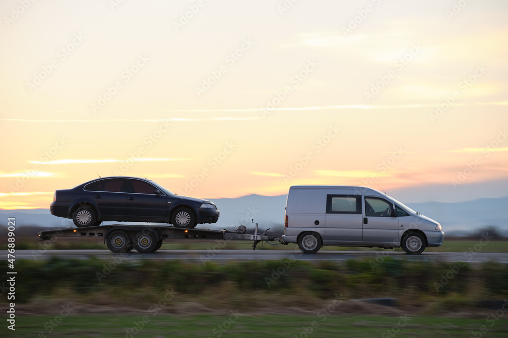 Tow truck vehicle with car transporting carrier trailer driving on highway in evening Tow truck vehicle with car transporting carrier trailer driving on highway in evening