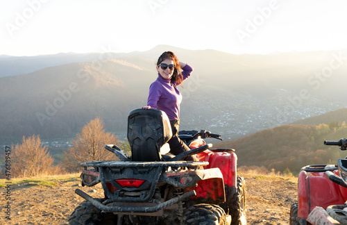 Young happy female driver enjoying extreme ride on ATV quad motorbike in fall mountains at sunset.