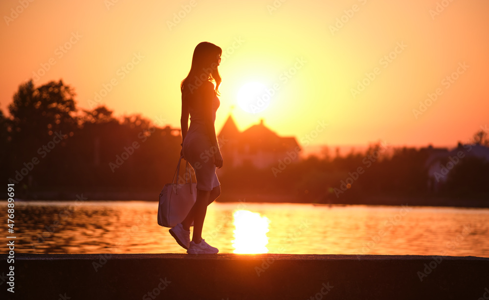 Young woman walking alone on lake shore walkway on warm evening. Solitude  and relaxing in nature concept Stock Photo | Adobe Stock