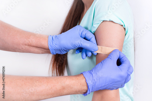 Doctor or nurse glues bandage on patient's shoulder after an injection or vaccination. Close-up. Vaccination against flu, pandemic coronavirus. Mandatory prevention of people for immunity from virus.