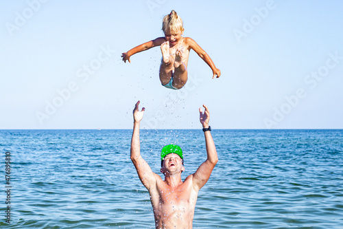 Young man dad tosses the baby girl up on the beach. Fototapet