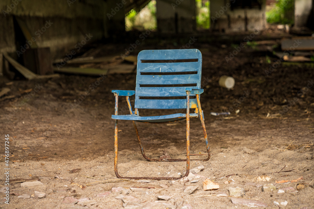 An old plastic folding chair in front of a derelict storehouse An old plastic folding chair in front of a derelict storehouse