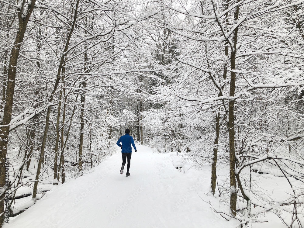 Man does jogging in a winter forest, running on snow-covered road, outdoor activities, healthy life