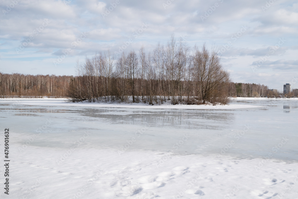 Early spring landscape of lake with surface covered with melting snow and small island with bare trees in the distance Early spring landscape of lake with surface covered with melting snow and small island with bare trees in the distance
