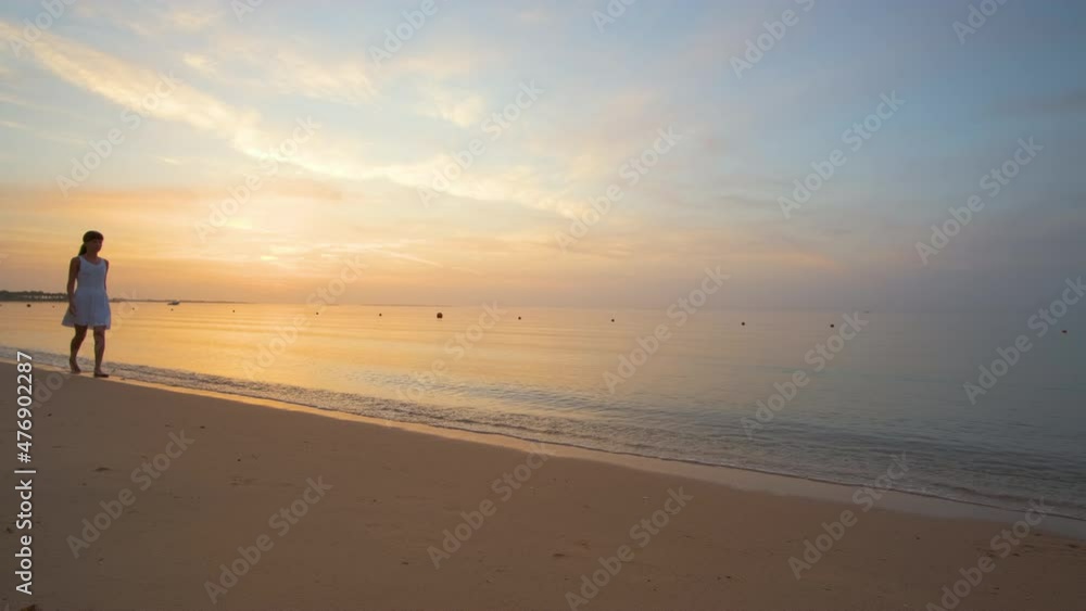 Young woman walking alone on sandy beach by seaside enjoying warm tropical evening Young woman walking alone on sandy beach by seaside enjoying warm tropical evening