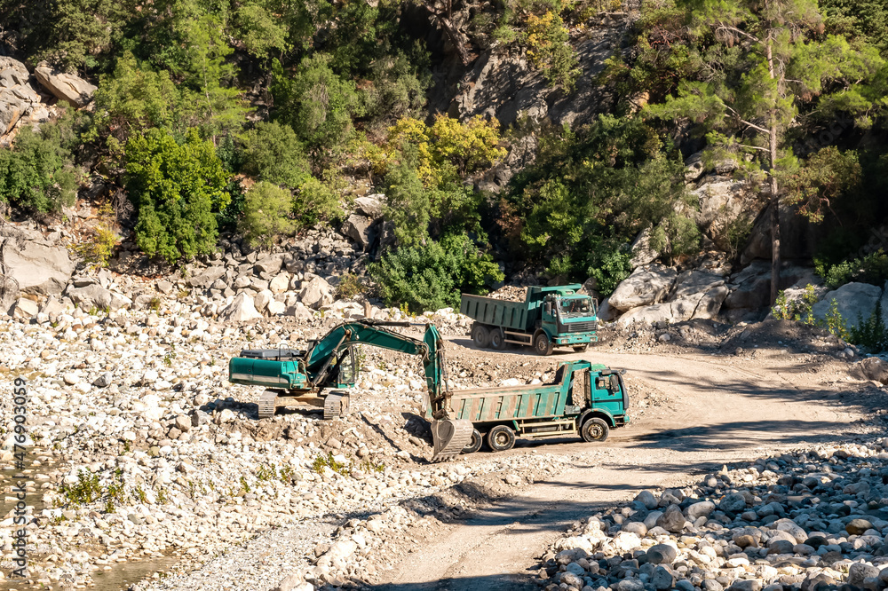 road works in the river valley, excavator and dump trucks move stones