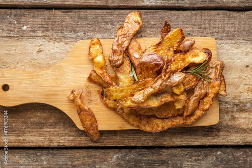 Crispy fried potato peel chips with rosemary and salt, top view, wooden background.