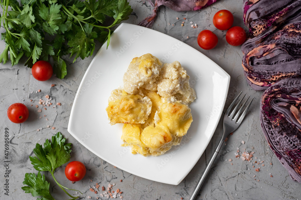 Delicious lunch for the whole family: cauliflower baked with cheese in cream sauce on a white plate on a gray background. Top view Delicious lunch for the whole family: cauliflower baked with cheese in cream sauce on a white plate on a gray background. Top view