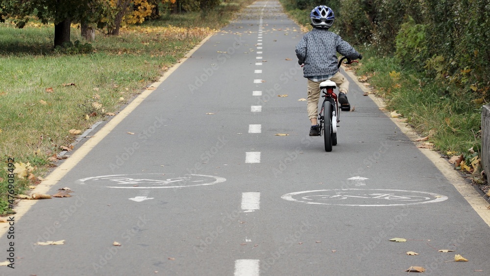 Little boy in a helmet on a bicycle rides on a bike path in the park