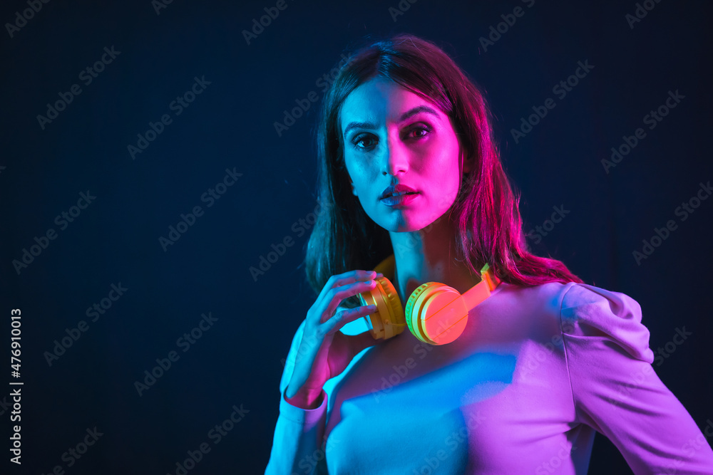 Young caucasian girl with yellow headphones on a black background, illuminated in a disco with neon lights Young caucasian girl with yellow headphones on a black background, illuminated in a disco with neon lights