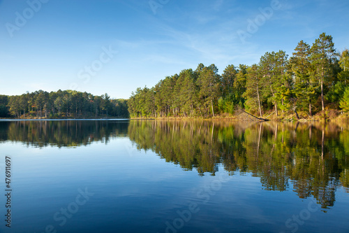 Foto Beautiful calm northern Minnesota lake under blue sky with trees along the shore