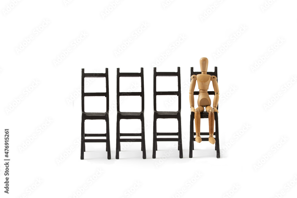 A wooden mannequin sits on a black chair on a white background. A minimal conception of a person who is exhausted, tired, depressed, desperate. Waiting. Puppet posture. A wooden mannequin sits on a black chair on a white background. A minimal conception of a person who is exhausted, tired, depressed, desperate. Waiting. Puppet posture.