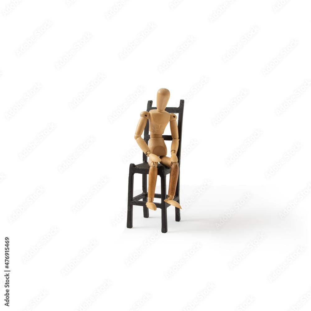 A wooden mannequin sits on a black chair on a white background. A minimal conception of a person who is exhausted, tired, depressed, desperate. A wooden mannequin sits on a black chair on a white background. A minimal conception of a person who is exhausted, tired, depressed, desperate.