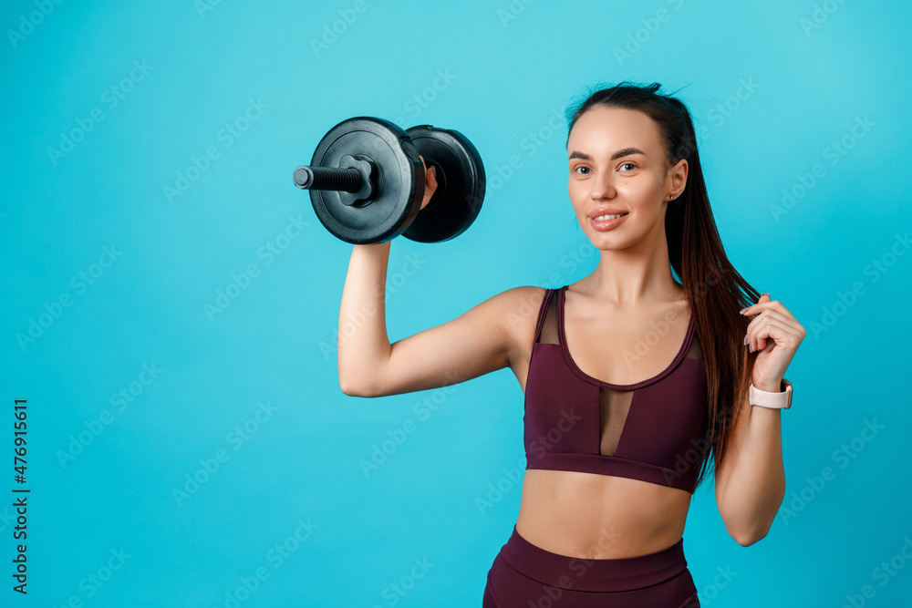 beautiful sportive brunette girl holding dumbbells on a blue background. charger. isolated beautiful sportive brunette girl holding dumbbells on a blue background. charger. isolated