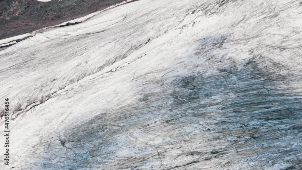 Large high grey cliffs with blue shadow rifts and big deep cracks covered with snow and black mineral products aerial view Large high grey cliffs with blue shadow rifts and big deep cracks covered with snow and black mineral products aerial view