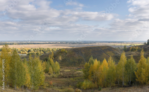 A view of the meadows and the endless expanse of the countryside. Autumn landscape with a river in the distance. The sun shines through the clouds on the fields and hills in an autumn day.