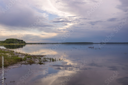 Evening landscape on the lake in early spring. The dramatic sky is reflected in the water. © Sergei