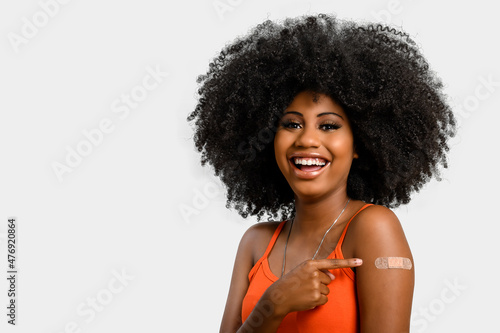 Fotografie, Obraz Black teen girl smile and points to her arm with vaccine sticker, she does not wear face shield, isolated on gray background