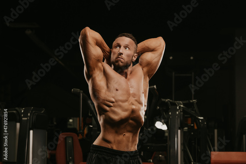 A bodybuilder with a beard is doing a stomach vacuum pose during a workout.