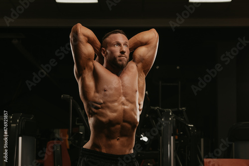 A bodybuilder with a beard is doing a stomach vacuum pose during a workout.