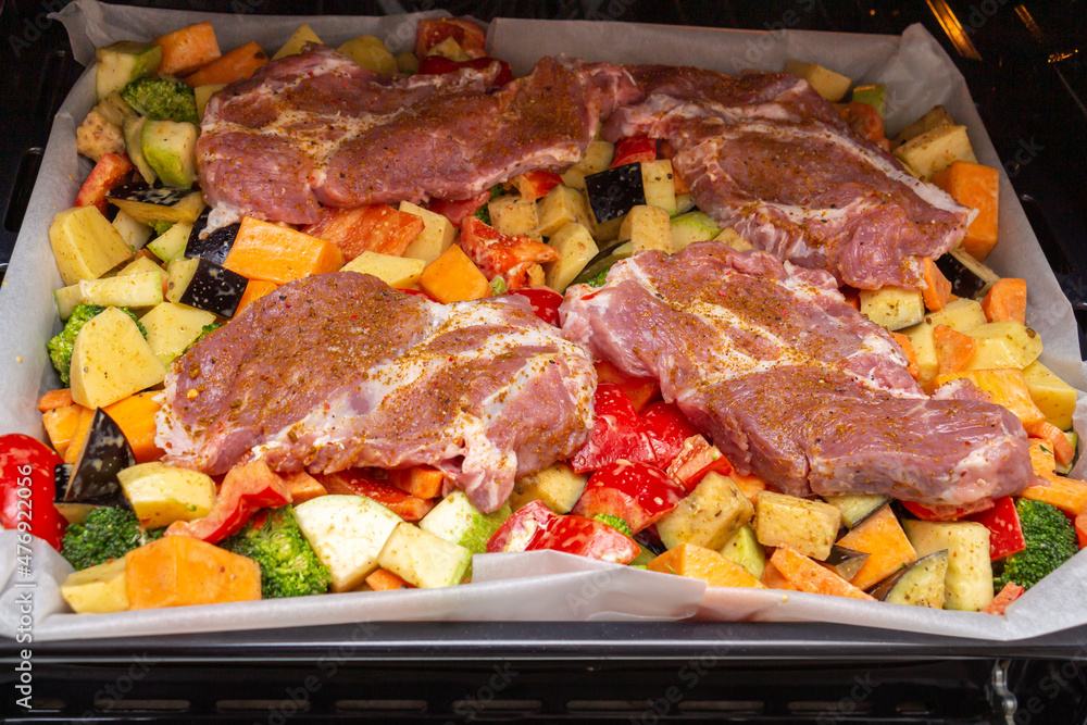 Finely chopped and seasoned vegetables with pork, placed on a baking sheet, before baking on parchment in the oven. Potatoes, bell peppers, squash, pumpkin and broccoli. Close-up