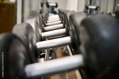Close-up of dumbbells on rack in sport fitness center background. Steel dumbbell set. Workout training and fitness gym concept. Healthy and well being concept. Sport equipment and tool theme