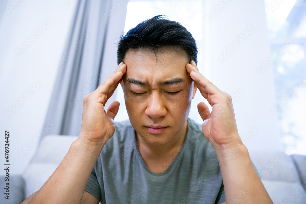 Young man suffering from headache after hard working day, sitting on couch at home