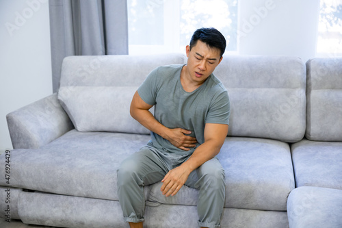 Canvas Print Casual man sitting on a couch at home complaining suffering belly ache