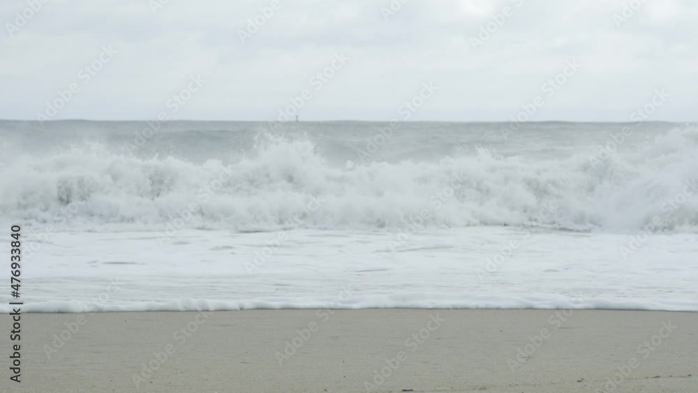 Distant waves crashing hard onto the surf, making a loud flop and splash noise onto the wet sand, during an offshore tropical storm causing a surge in tidal force Distant waves crashing hard onto the surf, making a loud flop and splash noise onto the wet sand, during an offshore tropical storm causing a surge in tidal force