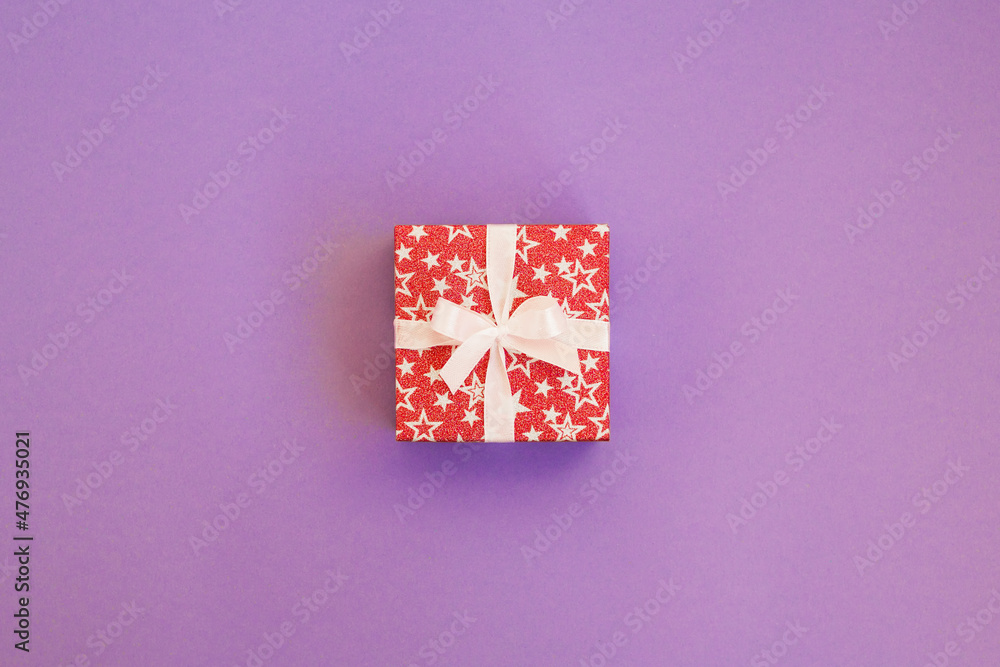 Gift box wrapped in red shiny paper with white ribbon on purple background. Mockup with copy space. Gift box wrapped in red shiny paper with white ribbon on purple background. Mockup with copy space.