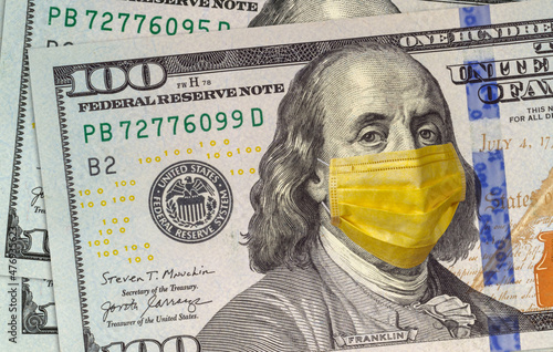 COVID-19 coronavirus in the USA and the world. Yellow medical mask on Benjamin Franklin's face on a hundred-dollar bill. The concept of protecting money from the crisis.