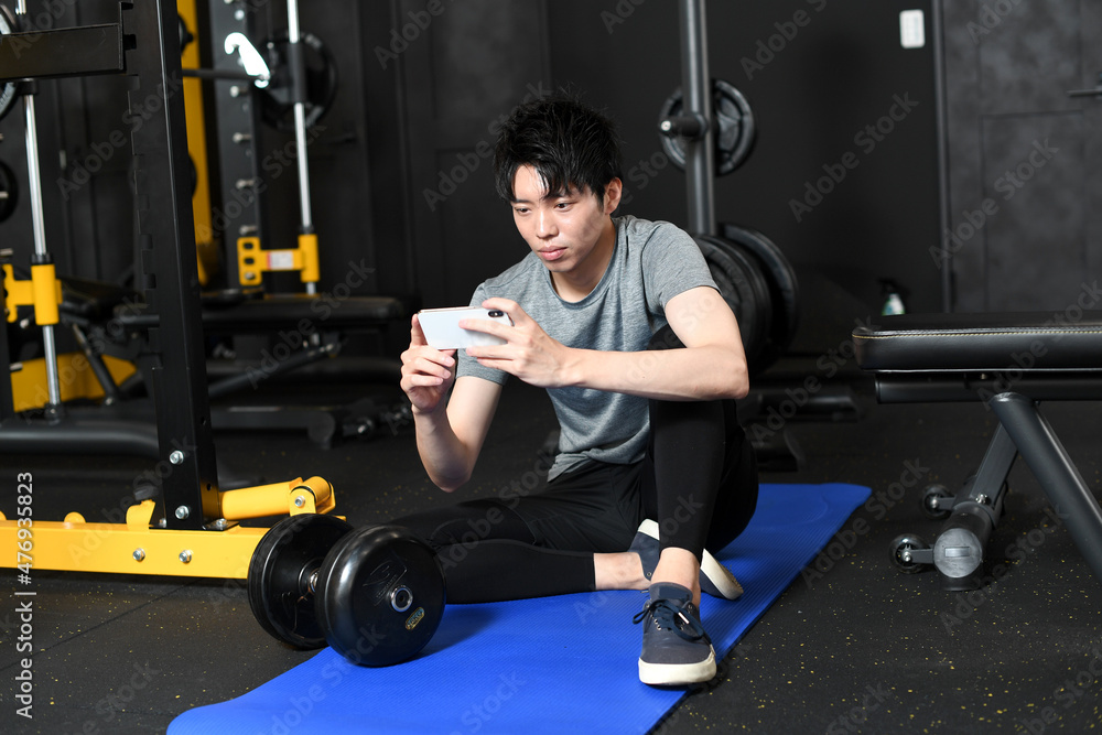 スマホアプリで健康管理をするジムにいる若い男性 スマホアプリで健康管理をするジムにいる若い男性