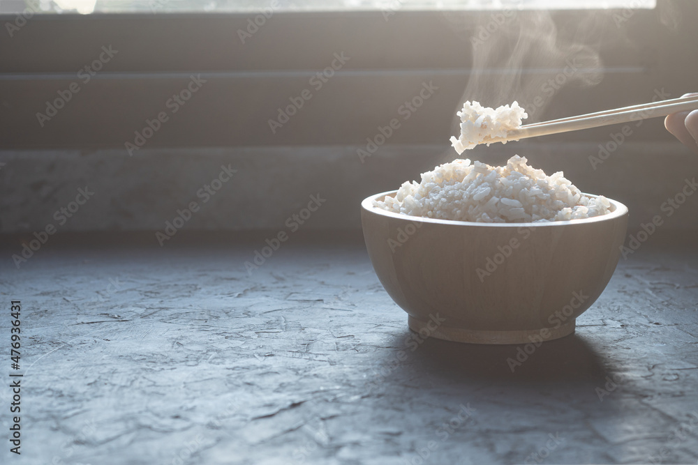 The man hand of using black chopsticks holding hot jasmine rice with smoke and steam in black bowl over dark background.hot food concept The man hand of using black chopsticks holding hot jasmine rice with smoke and steam in black bowl over dark background.hot food concept