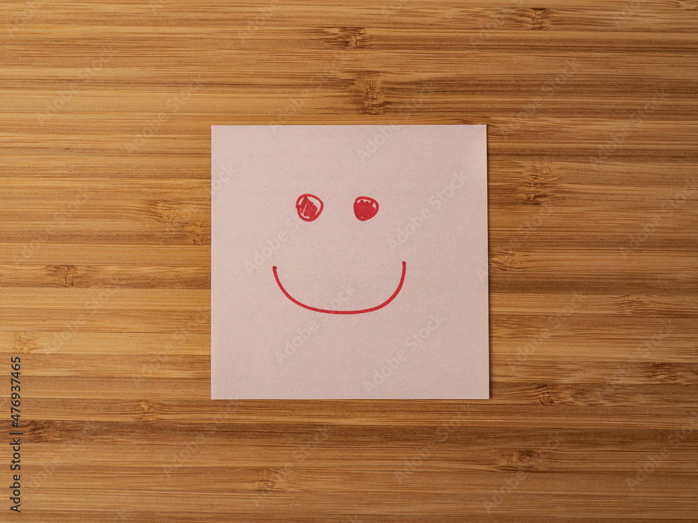A paper sticker pasted on a wooden surface with the image of the happy smiley character