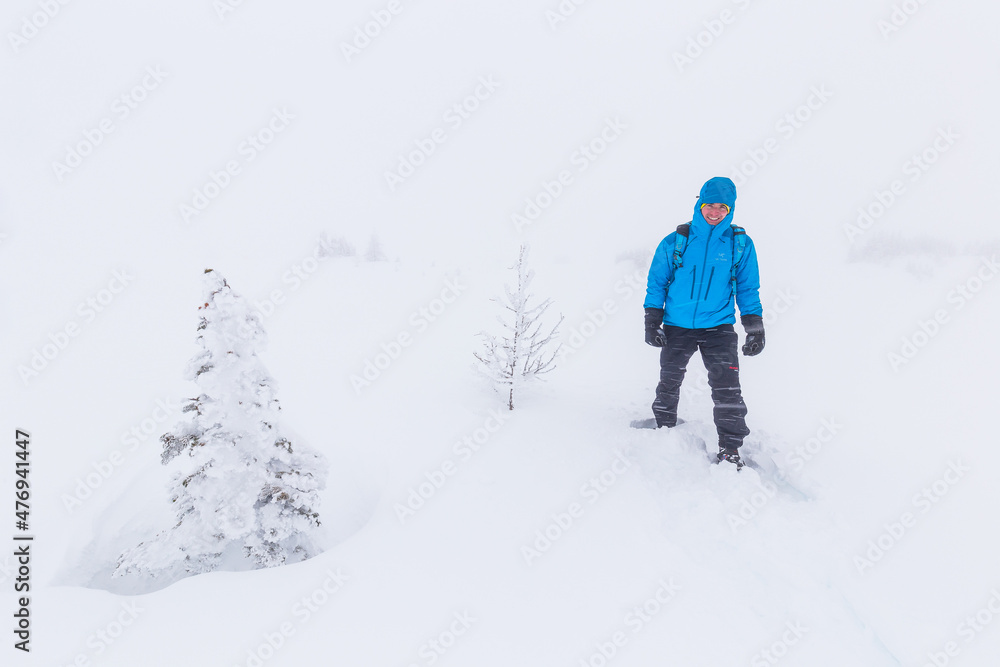 Hiker snowshoeing through high contrast trees in a snow storm fog