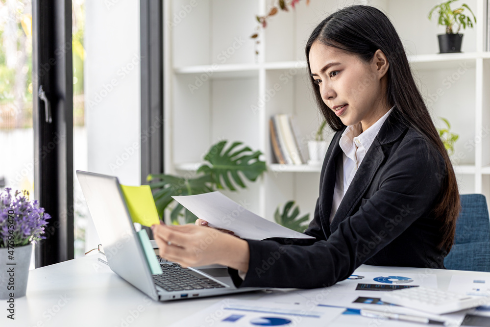 Woman working in a private office, a business woman owner of a company holding a notepad with notes on her laptop, she is checking company financial documents. Concept of company financial management. Woman working in a private office, a business woman owner of a company holding a notepad with notes on her laptop, she is checking company financial documents. Concept of company financial management.