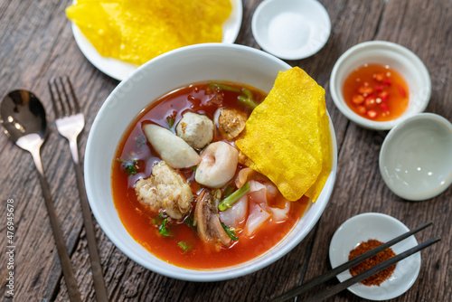 Red Sauce Noodle Soup called Yentafo Noodle, Thailand Street Food, noodle with fish meatballs, tofu and fried wonton plates serving with seasonings on wooden vintage table